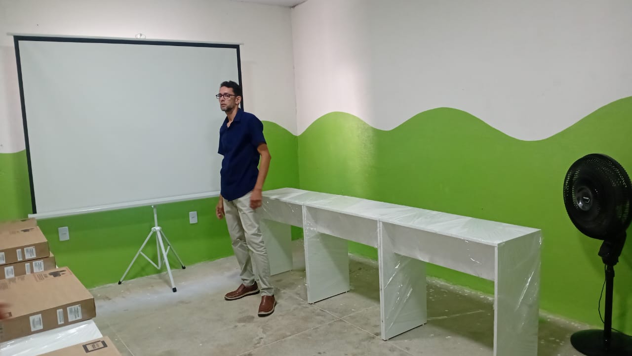 Sala de informática preparada com mesas e tela de projeção